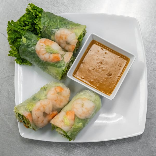 Four fresh spring rolls with shrimp and lettuce, served with a side of peanut sauce.