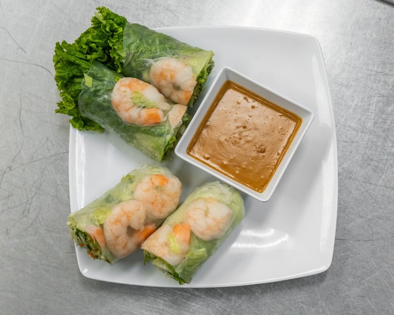 Four fresh spring rolls with shrimp and lettuce, served with a side of peanut sauce.
