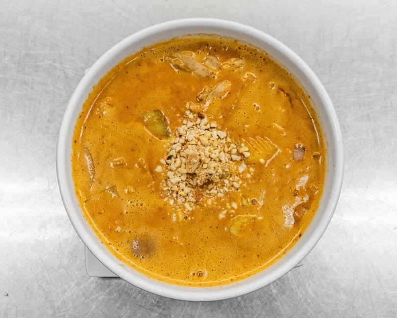 Overhead view of a bowl of orange curry with chicken, vegetables, and crushed peanuts.