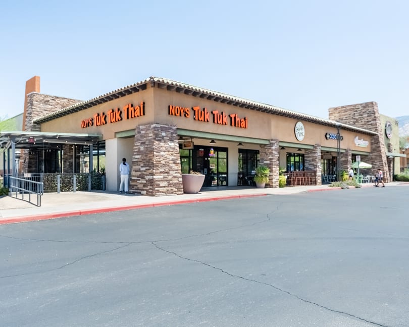Exterior of Noy's Tuk Tuk Thai restaurant, a tan building with stone accents and orange signage.