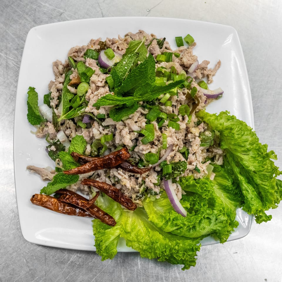 Larb, a Thai minced meat salad with herbs, red onion, and dried chilies on a white plate.
