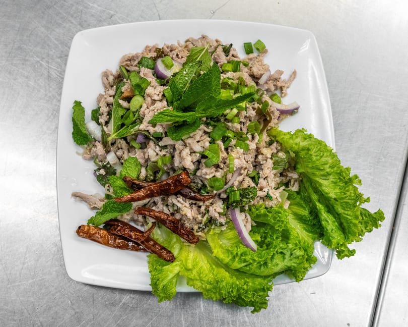 Larb, a Thai minced meat salad with herbs, red onion, and dried chilies on a white plate.