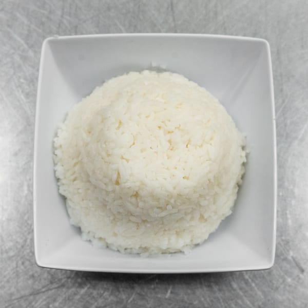 A white square bowl filled with fluffy white rice, centered on a metallic surface.