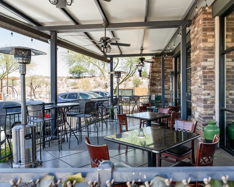 Outdoor patio dining area with various tables, chairs, and heaters under a covered roof.