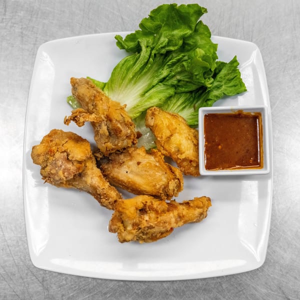 Crispy fried chicken wings with fresh lettuce and a side of dipping sauce on a white plate.