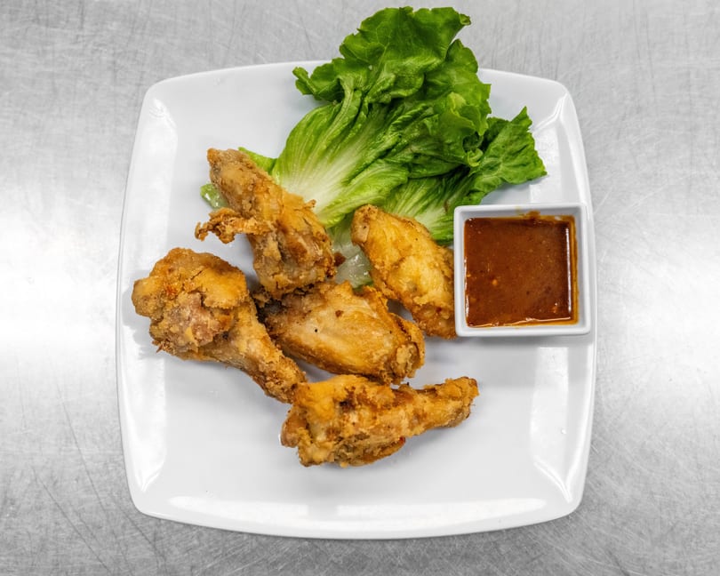 Crispy fried chicken wings with fresh lettuce and a side of dipping sauce on a white plate.