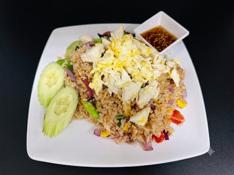 Crab fried rice with scrambled egg, cucumber slices, and a side of chili sauce.