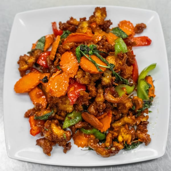 Crispy chicken stir-fry with carrots, bell peppers, and basil on a white rectangular plate.