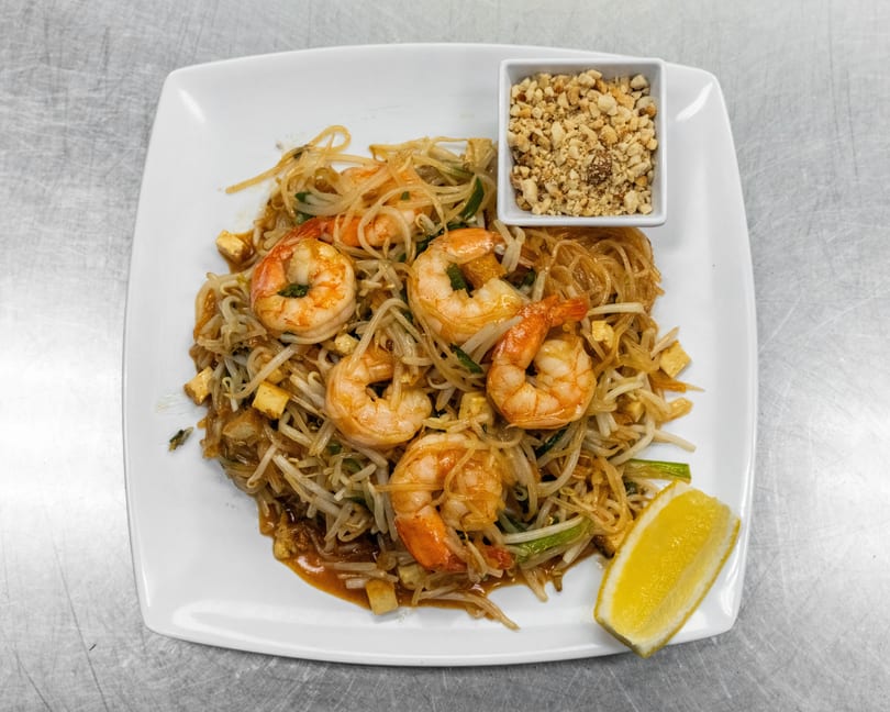 Shrimp Pad Thai with noodles, bean sprouts, tofu, crushed peanuts, and a lemon wedge.