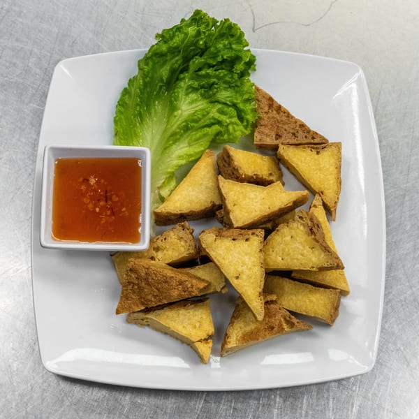 Crispy fried tofu triangles with a side of sweet chili dipping sauce and a lettuce leaf.