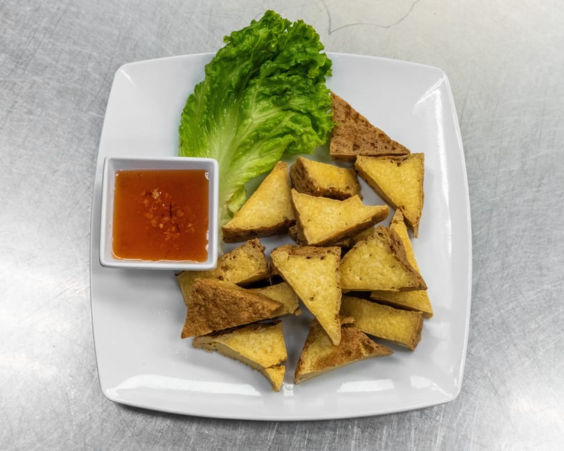 Crispy fried tofu triangles with a side of sweet chili dipping sauce and a lettuce leaf.